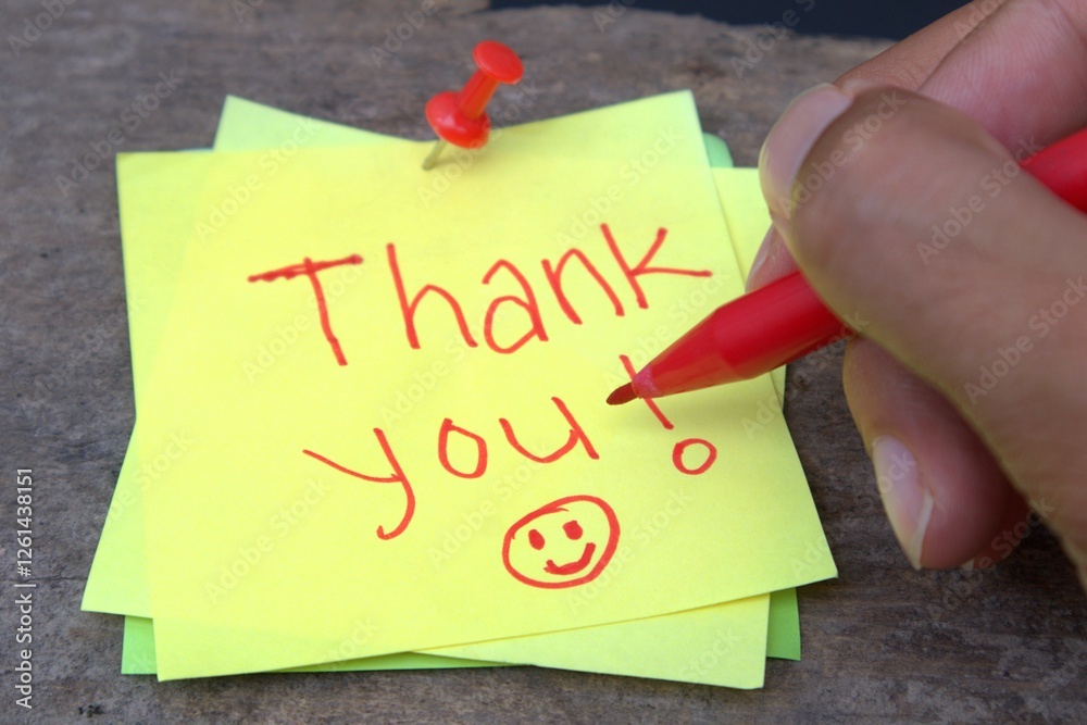 Hand holding a marker writing the word ''thank you'' on a yellow Sticky note Hand holding a marker writing the word ''thank you'' on a yellow Sticky note