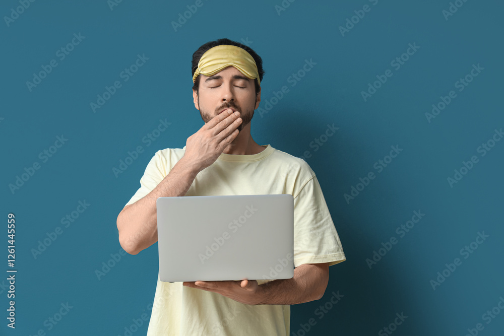 Sleepy young man with sleep mask and laptop yawning on blue background Sleepy young man with sleep mask and laptop yawning on blue background