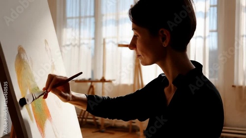 An artist seated in a bright studio, slowly adding soft brushstrokes to a large canvas.