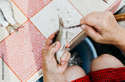 An elderly woman cleans fish from scales at the table. photo