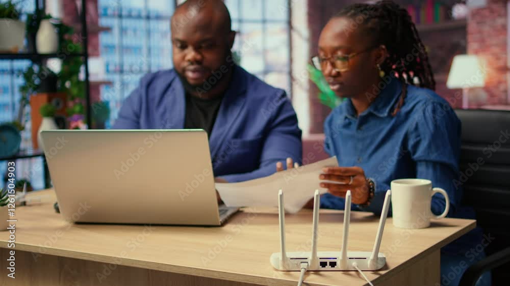 Black irritated man and woman rebooting their wireless router and checking network settings, feeling angry with the struggles to resolve an internet outage disrupting their tasks. Camera A.