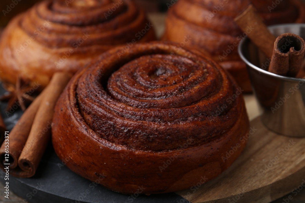 Fototapeta premium Delicious cinnamon roll buns and spices on wooden table, closeup