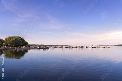 Sunny afternoon view of Lake Scugog with a row of yachts and people on the pier in Port Perry Marina. Port Perry is a community located in Scugog, Ontario, Canada 84 kilometres northeast of Toronto.