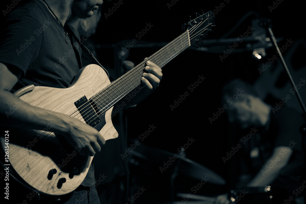 Fototapeta premium Close-up of guitarist performing with a drummer blurred in the background.