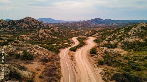 A winding dirt road through rocky hills under a cloudy sky.