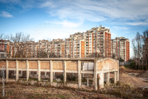 An abandoned industrial structure stands before towering communist-era apartment blocks. in Pancevo, serbia This stark scene highlights bankruptcy, shifting economies, and urban transition. photo