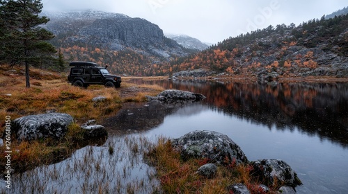 Black off-road vehicle parked on the shore of a calm mountain lake surrounded by autumn foliage under a cloudy sky.