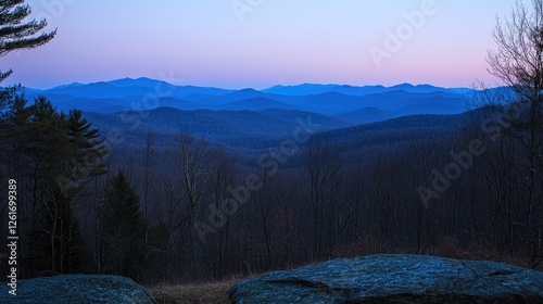 Serene twilight view of layered mountains with fading light and sparse trees in the foreground