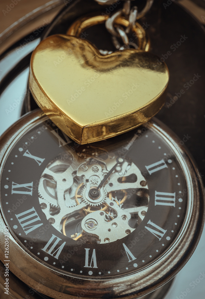 Close-up of Golden heart shaped love padlock lap over A retro pocket watch. Love can endure beyond the limitations of time, Concept of Love that transcends time, Valentine's day, Space for text.