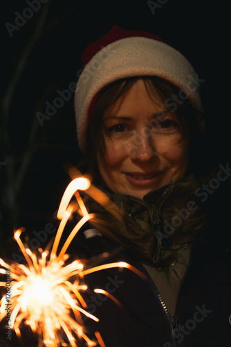 Obraz na płótnie Girl painting with freeze light. Festive freezing lights in the night. Sparkling forms made by woman in Santa hat. Stop light drawings. New Year fun. Firework background. Freeze light symbol in motion w salonie