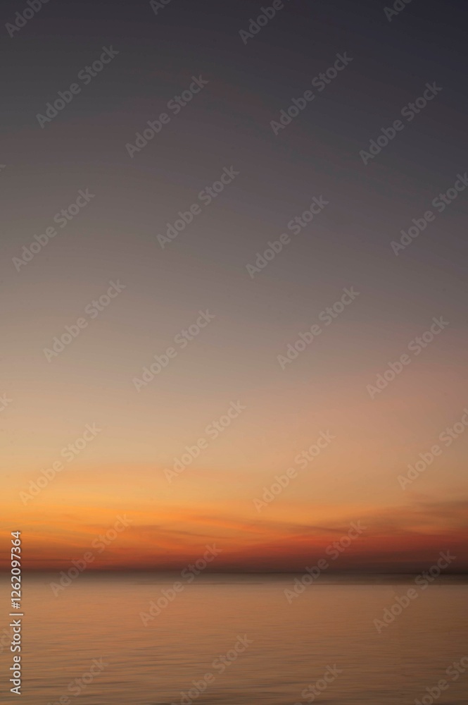 Naklejka premium Soft gradient sunset over calm ocean waters with a vast sky