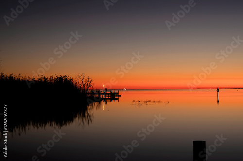 Fototapeta Naklejka Na Ścianę i Meble -  Tranquil sunset over a calm lake with reflections and a wooden dock