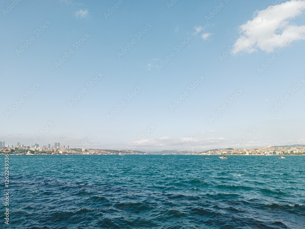 Obraz premium A view of the Bosphorus Strait in Istanbul, with boats scattered across the deep blue water. The city's skyline and buildings are visible in the distance under a clear sky