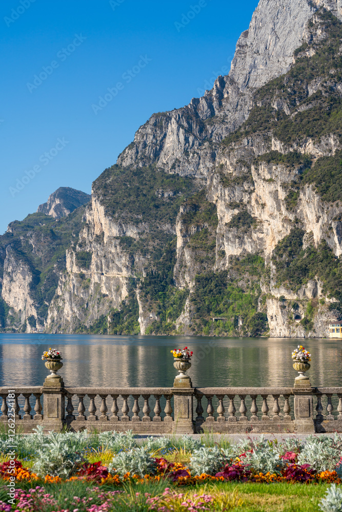 Riva del Garda, Italy: Scenic lakefront with flowers, mountains, and a stone balustrade.