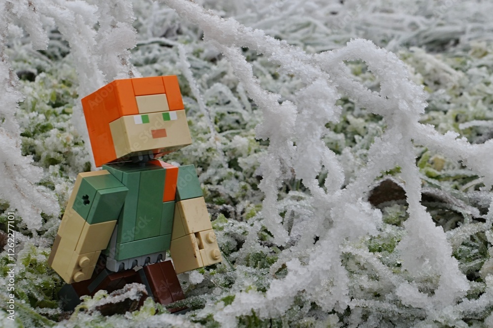 Fototapeta premium LEGO Minecraft figure of Alex adoring heavy icing on winter tree branches, frozen grass in background.