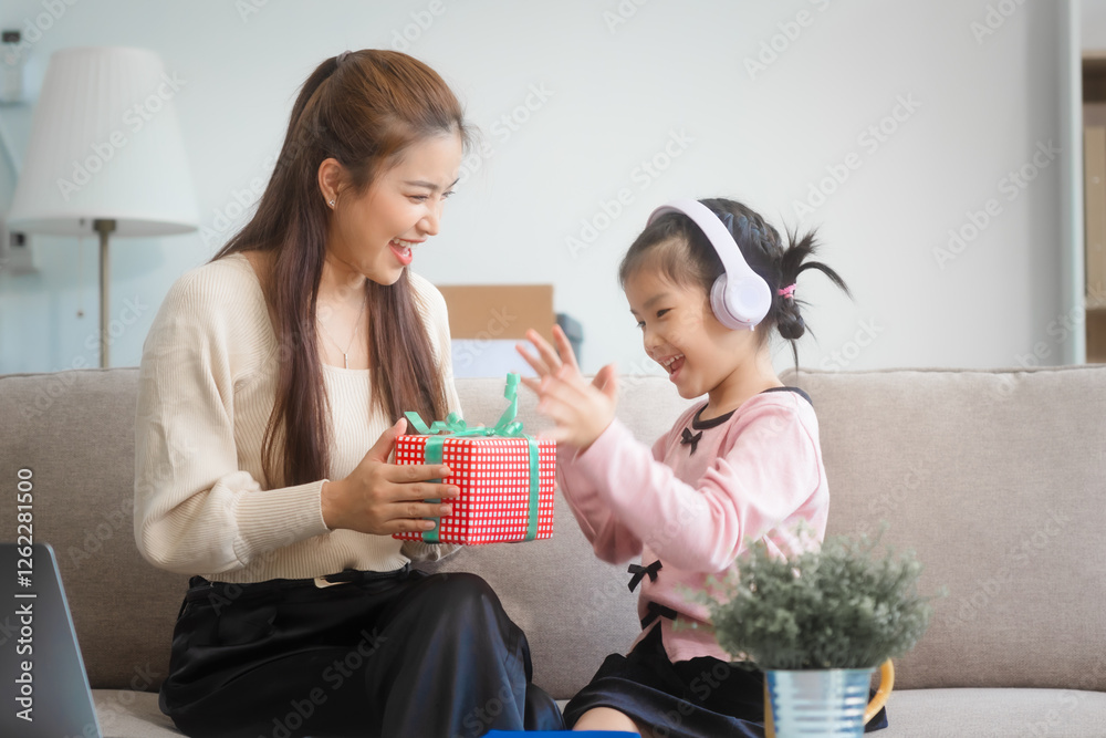 Asian young mother and her daughter sit together on the sofa in the cozy living room, working on homework at the desk, creating a warm and supportive atmosphere for learning, love, hug, mother days.