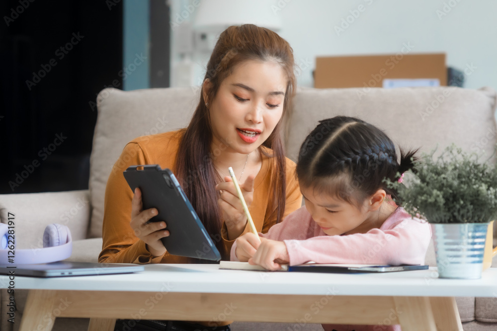 Asian young mother and her daughter sit together on the sofa in the cozy living room, working on homework at the desk, creating a warm and supportive atmosphere for learning, love, hug, mother days. Asian young mother and her daughter sit together on the sofa in the cozy living room, working on homework at the desk, creating a warm and supportive atmosphere for learning, love, hug, mother days.