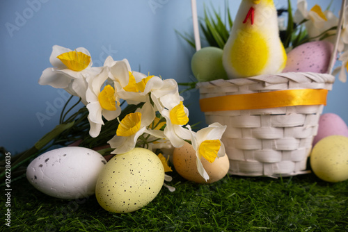 Colorful eggs and daffodil close up, chicken and eggs in a white basket on green grass Blue background photo