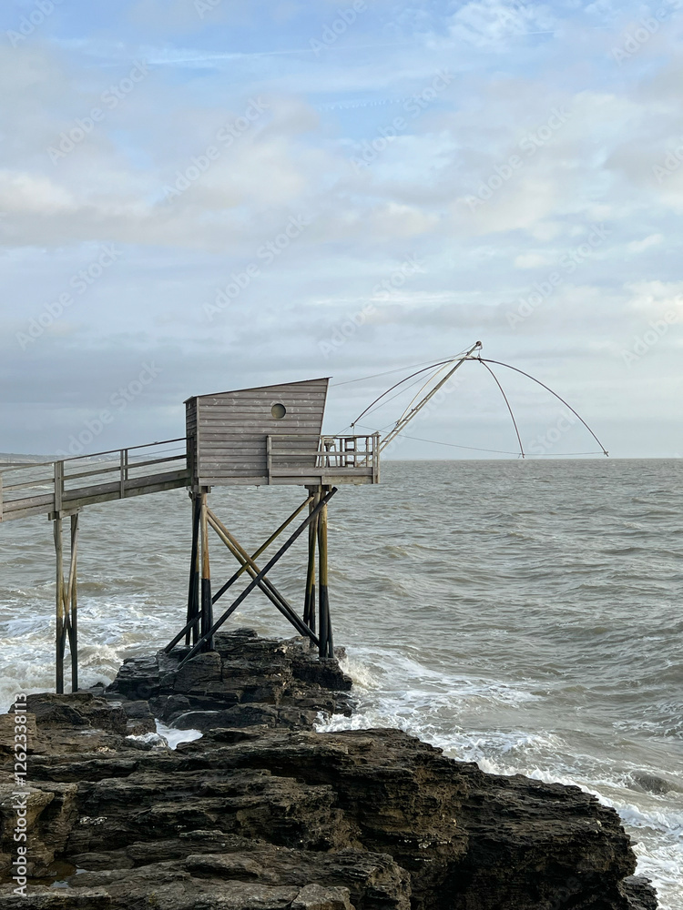 Traditional French fishing hut on stilts with carrelet net over ocean. Wooden structure stands on rocky shore, with waves and cloudy sky. Ideal for projects to travel, culture, or traditional fishing. Traditional French fishing hut on stilts with carrelet net over ocean. Wooden structure stands on rocky shore, with waves and cloudy sky. Ideal for projects to travel, culture, or traditional fishing.