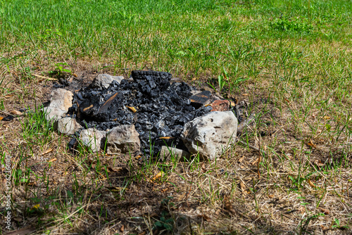 Εκτύπωση καμβά Fire pit remnants show ashen remains surrounded by stones in a grassy area on a