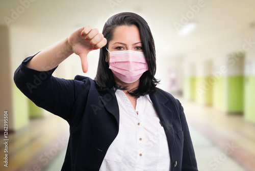 Businesswoman making thumb-down disagree gesture wearing mask photo