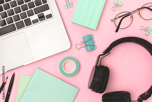 Workspace with laptop,headphones, eyeglasses and office supplies on a pink background. Workspace for online education. photo