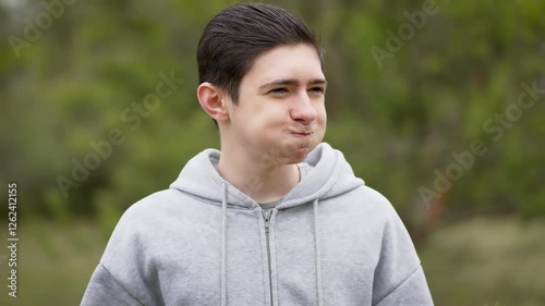 Cheerful playful teenage boy puffing cheeks with air and blowing it out with finger. Joyful adolescent fooling around. Happy young man acting silly, filling cheeks with air and blowing it out