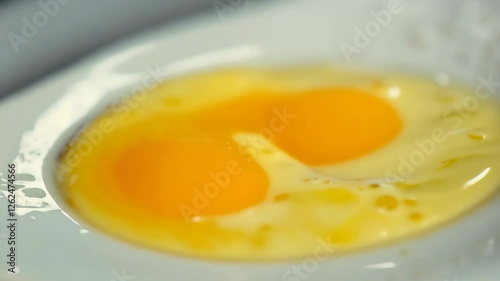 Close-up of a fresh egg yolk resting on a light gray plate, showcasing its vibrant color.