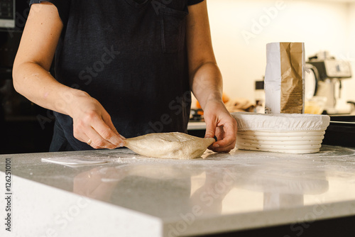 Schilderij op canvas Hands are skillfully rolling and shaping dough on a clean kitchen countertop sprinkled with flour, healthy sourdough bread