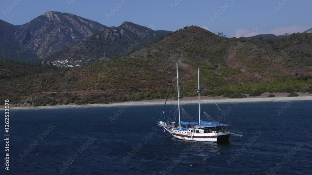 Sailing boat on deep blue waters near pristine beach, with mountain landscape in background, Karaincir, Turkey Sailing boat on deep blue waters near pristine beach, with mountain landscape in background, Karaincir, Turkey
