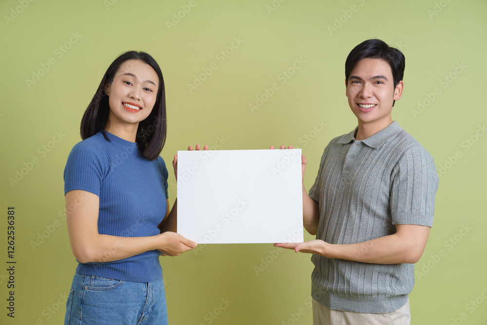 Young Asian couple holding a white board on green background Young Asian couple holding a white board on green background