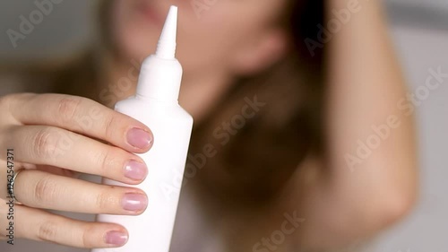 Close up of a female holding a white bottle of serum for head scalp, blurred background  photo