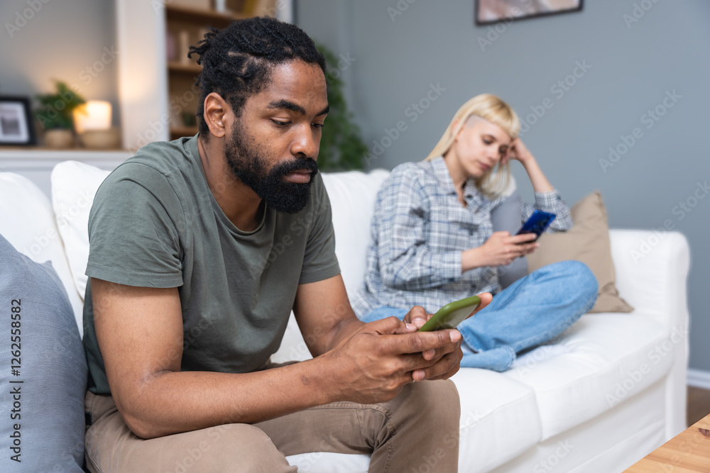 Fototapeta premium Gadget addiction and relationship problems. Couple with smart phones ignoring each other. Obsessed man and woman, roommates with their cell phones ignore each other sitting on a couch at home.