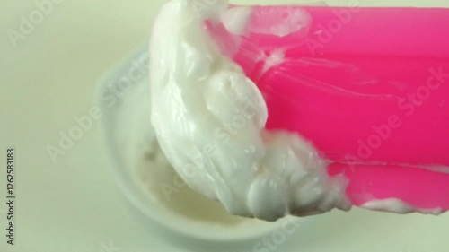 Macro shot of a cosmetic laboratory process where gloved hands in blue gloves mix a cream using a porcelain mortar and pestle. The scene showcases the precise formulation of a thick, high-consistency 