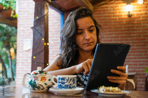 A young latin woman, Brazilian, sitting in concentration, studying on a tablet, looking focused on a tablet screen. photo