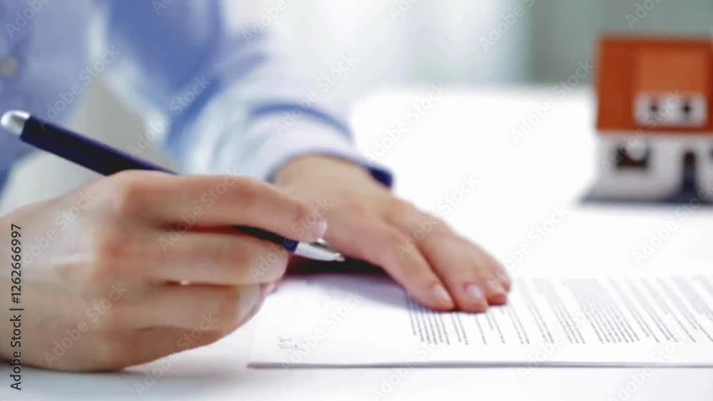 Businessman signing a contracts, with house model background. Businessman Signing Legal Paper In Office Real estate agent Businessman signing a contracts, with house model background. Businessman Signing Legal Paper In Office Real estate agent