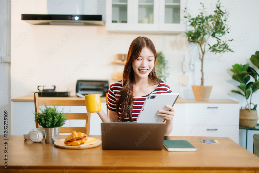 Asian woman working remotely on a laptop and tablet in a cozy kitchen workspace. Perfect for education Asian woman working remotely on a laptop and tablet in a cozy kitchen workspace. Perfect for education