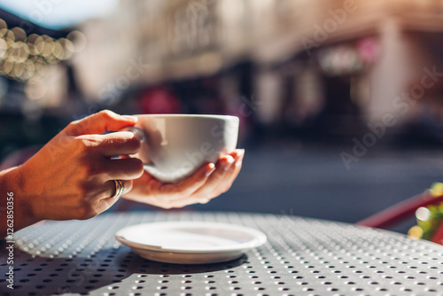 Close up of cup of coffee in female hands. Woman drinking hot beverage in outdoor cafe at sunset. Space photo