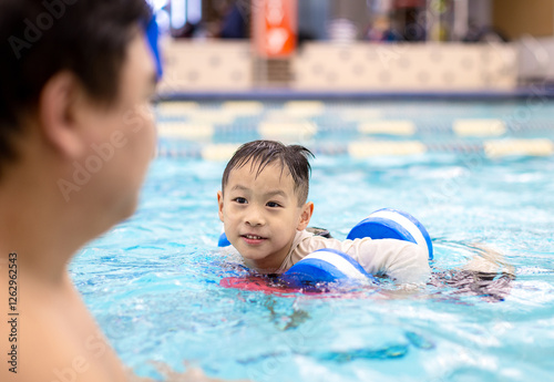 Man is watching a child swim in a pool
