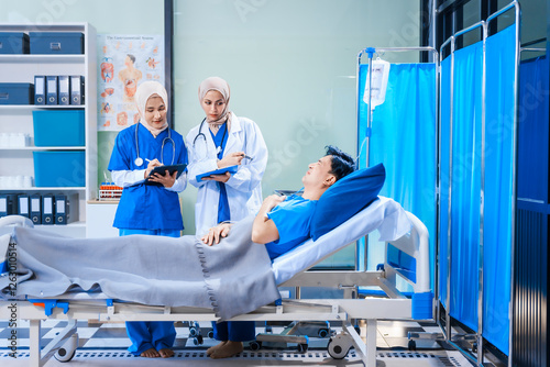 Asian middle-aged man patient rests in a hospital bed while a middle-aged Muslim woman doctor and a middle-aged Asian woman nurse check for diseases like flu and pneumonia, ensuring his recovery. photo