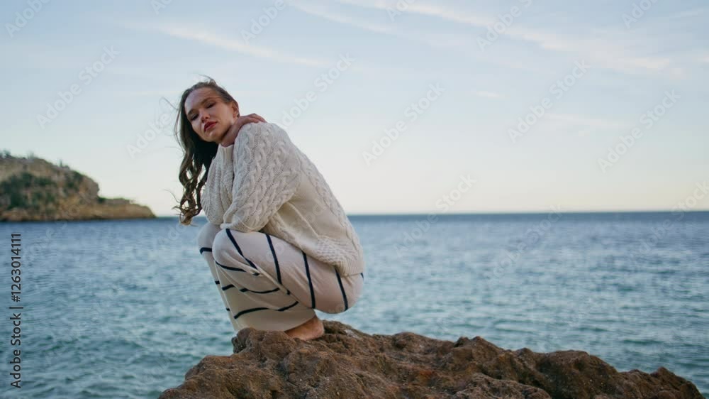 Beautiful model posing seascape crouching on coastal rock. Woman enjoying ocean Beautiful model posing seascape crouching on coastal rock. Woman enjoying ocean