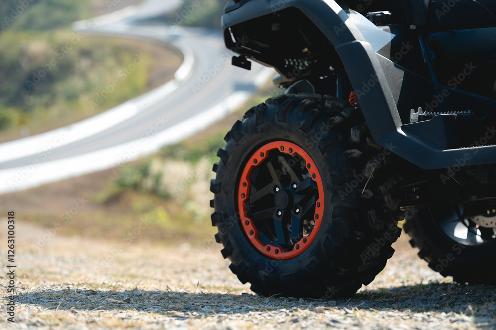 A close-up of a rugged tire from an all-terrain vehicle, showcasing bold design and vibrant orange accents against a blurred winding road backdrop. A close-up of a rugged tire from an all-terrain vehicle, showcasing bold design and vibrant orange accents against a blurred winding road backdrop.
