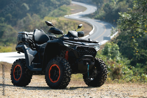 A sleek black ATV parked on a dirt path near a winding road, surrounded by lush greenery and hills, perfect for off-road adventures.