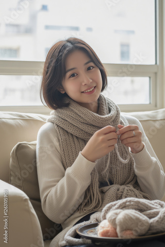 A Japanese teenage girl knitting a scarf while seated near a large window in a sunlit living room photo