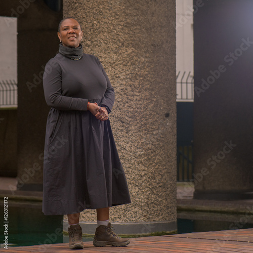 Londres, Reino Unido, 13 Feb 2025 – Retrato de una mujer con vestido negro y botas de senderismo posando en el Barbican Centre, una icónica obra de la arquitectura brutalista en Londres. photo