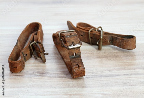 Old leather straps used to tie up skis together. Natural leather belts on wooden table. photo