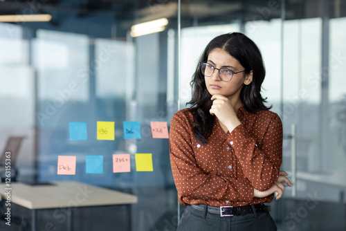 Fotografie Serious thinking woman at workplace inside office standing near window