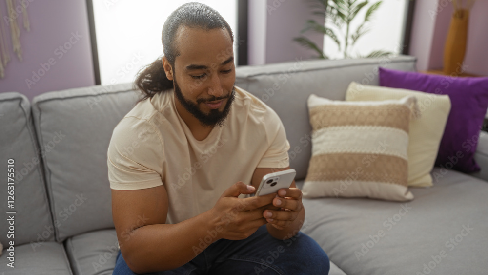 Young man with beard relaxing indoors holding smartphone in cozy apartment interior with modern decor casual style. Young man with beard relaxing indoors holding smartphone in cozy apartment interior with modern decor casual style.