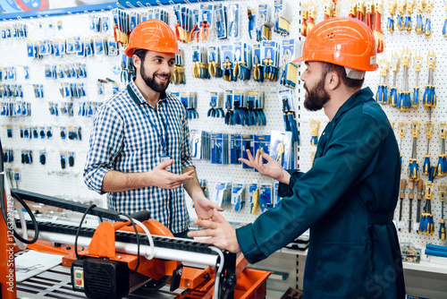 Two salesmen are discussing equipment selection near woodworking machine in power tools store.