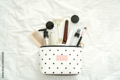 A chic, stylish polkadotted beauty bag filled with essential hair and skin care products resting on a white bed. photo